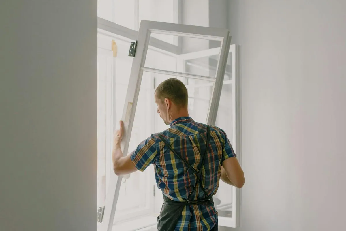 Installer lifting a new white window sash into place inside a bright room