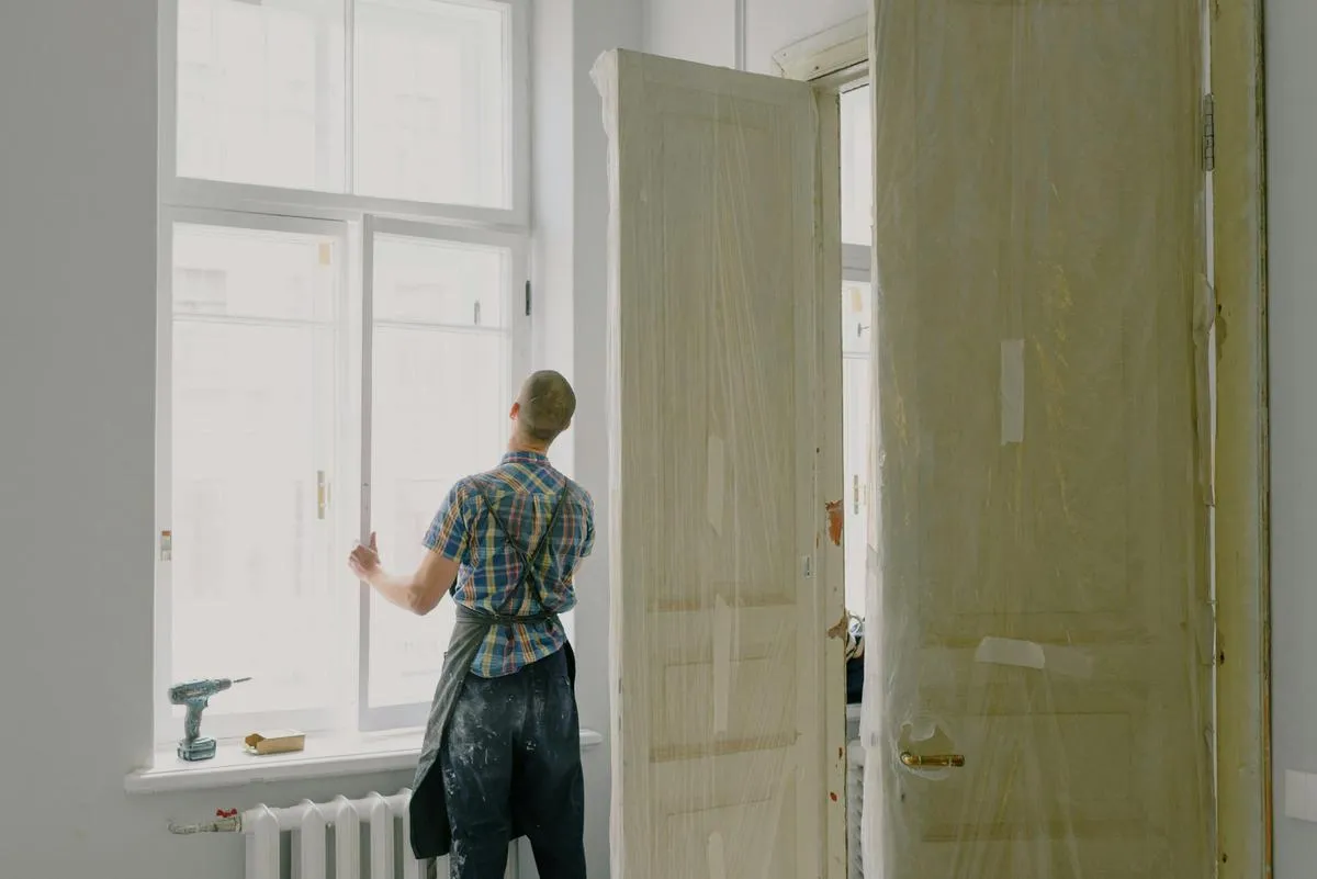 Worker opening an older white wood window to check the sash and hardware